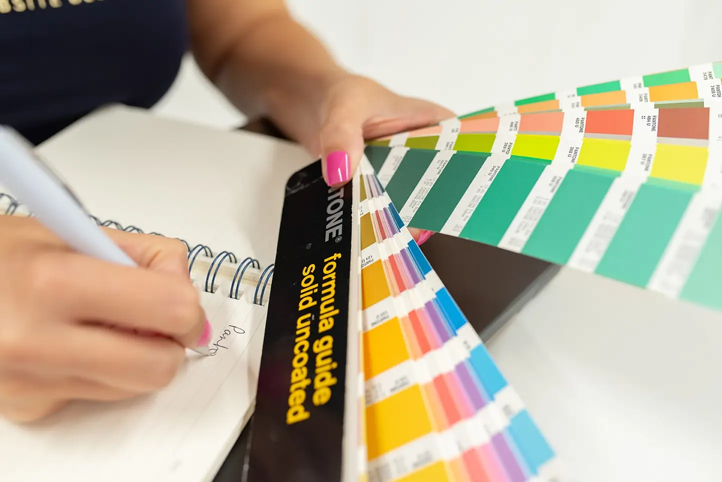 Liz owner of Bit2Flash website design Chelmsford is holding a fanned out Pantone colour chart and is writing in a notebook