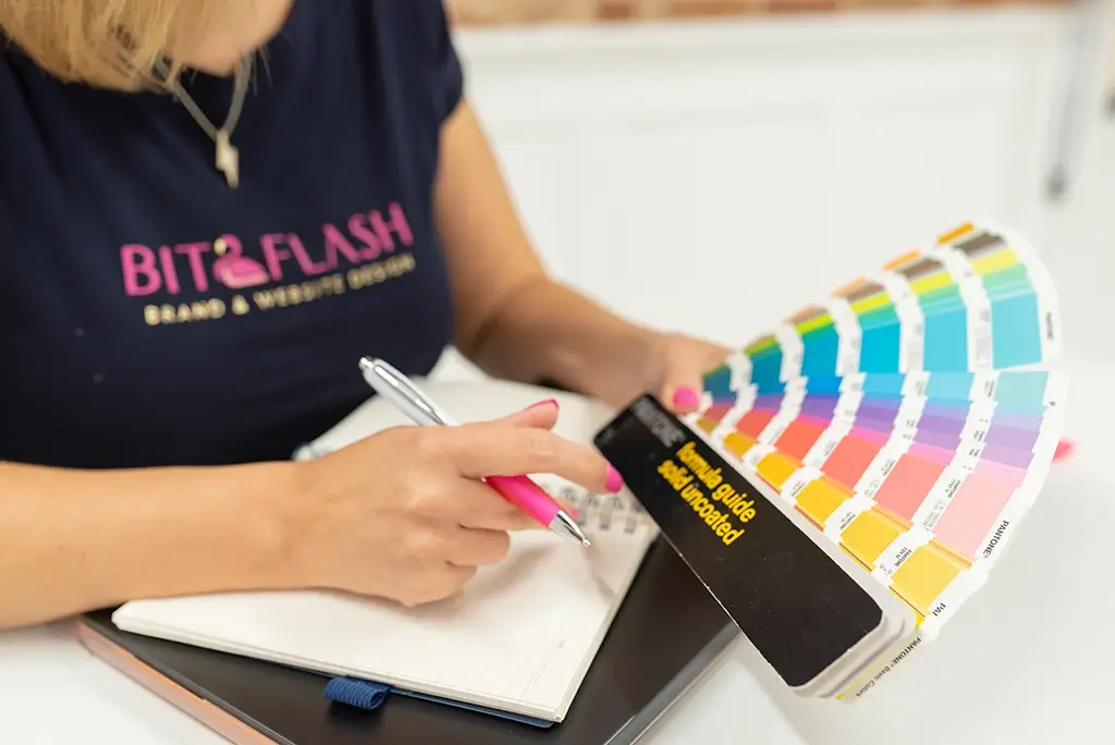 Liz owner of Bit2Flash website design Chelmsford is holding a fanned out Pantone colour chart and is writing in a notebook